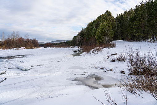 Flowing river at winter. Winter landscape with a River and Winter Forest. River with snow and ice in the winter woods. Selective focus.