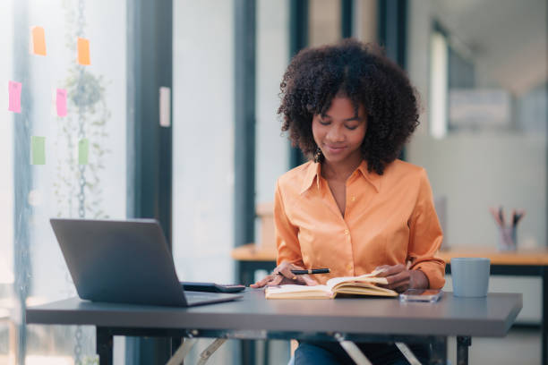 istock Young african american businesswoman using laptop computer, taking notes, working project in modern office. Financier working with documents at workplace. 1803472324
