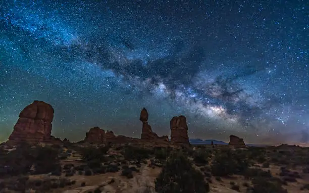 Iconic Balanced Rock and nearby sandstone rock formations silhouetted against the Milky Way in Arches National Park near Moab, Utah.