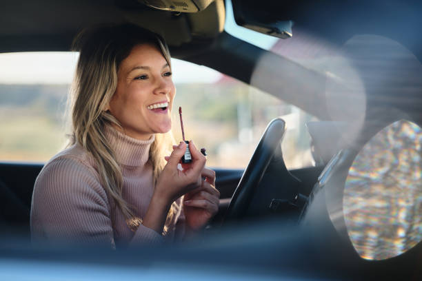 istock Happy woman applying lip gloss in a car. 1803502887