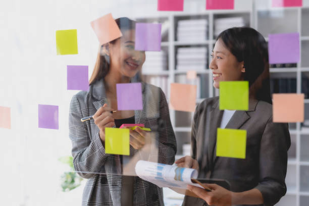 istock Two Asian business woman writing something on sticky notes while working on a business plan at office. 1803503439