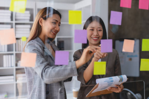 istock Two Asian business woman writing something on sticky notes while working on a business plan at office. 1803503502