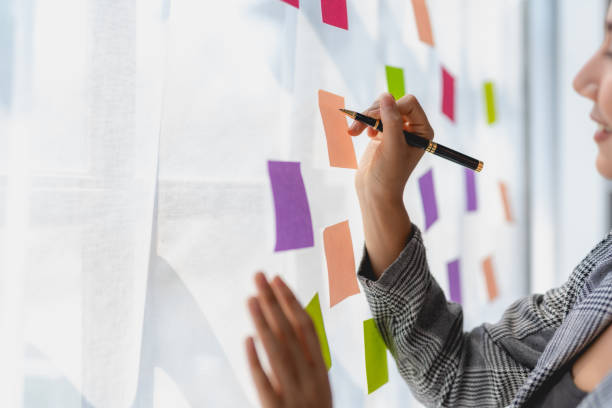 istock Asian business woman writing something on sticky notes while working on a business plan at office. 1803503979