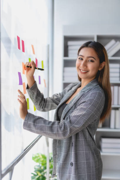 istock Asian business woman writing something on sticky notes while working on a business plan at office. 1803503986