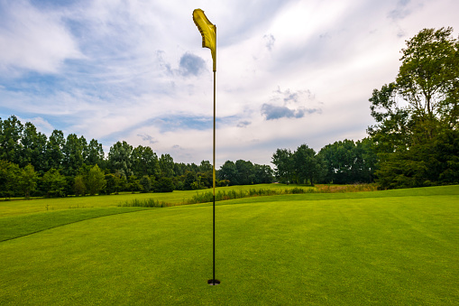 Golf course with yellow flag on 18th hole against a cloudy sky