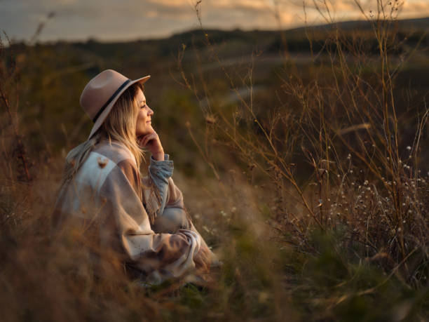 istock Relaxed woman day dreaming in tall grass on a hill. 1803509704