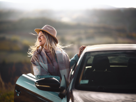 Carefree woman standing by the open car door during autumn day in nature. Copy space. Photographed in medium format.