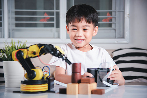 Happy Asian little kid boy using remote control playing robotic machine arm for pick up wood block, Funny child learning successful getting lesson control robot arm, Technology science education