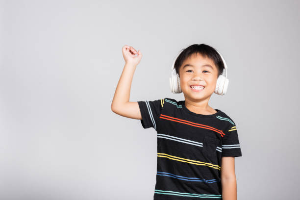 piccolo bambino carino di 5-6 anni ascolta musica in cuffie wireless in studio girato isolato su sfondo bianco, bambini asiatici felici che sorridono ascoltando audio e ballando, stile di vita di intrattenimento - one kid only audio foto e immagini stock