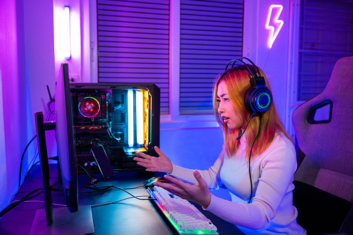 Game Over. Asian gamer playing online video game online she losing and sad on computer PC colorful neon LED lights, streamer woman in gaming headphones feeling disappointed about lost game, E-Sport
