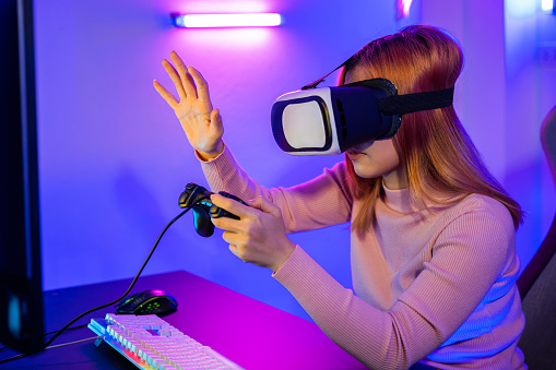 Gamer in VR headset glasses exploring metaverse plays online video game touching something on air and hold joystick, Excited woman playing watching video life simulation at home