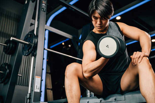 istock handsome young Asian man sitting on an exercise bench holding a heavy dumbbell 1803527745