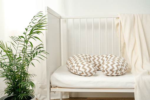 White wooden baby crib with pillow in nursery room close up