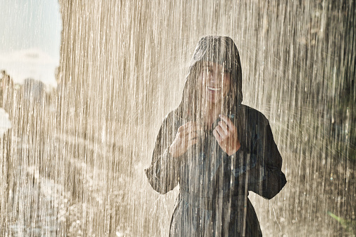 Happy woman in raincoat enjoying while standing on a rain in nature and looking at camera. Copy space.