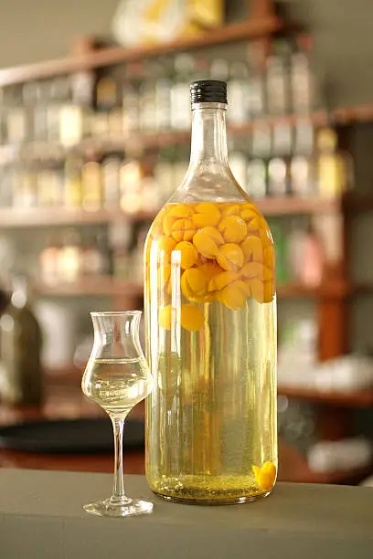 Bottle and cup of aguaymanto fruit (physalis peruviana), also known as peruvian ground cherry, macerated in peruvian pisco, on a blurry bar background.