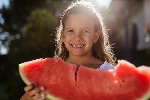 Beautiful girl enjoying summer eating watermelon in back yard.
