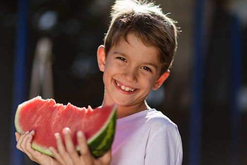 Beautiful boy enjoying summer eating watermelon in back yard.