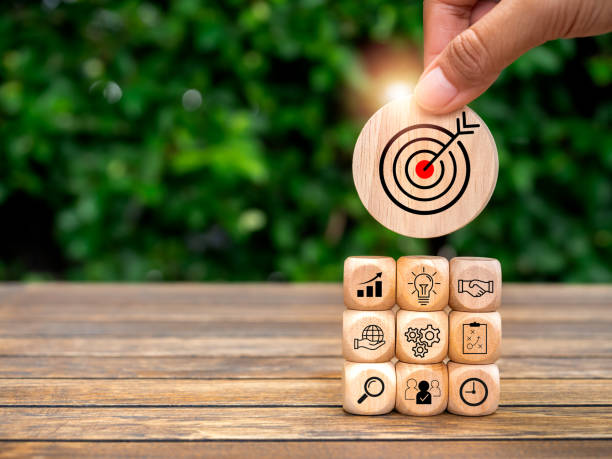 istock Business goal plan and growth success process for Leadership concept. Big target in hand put on top of wooden cube block stack with business strategy icon on desk and green background with copy space. 1803573904