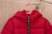 Child red puffer coat drying on hanger in bathroom