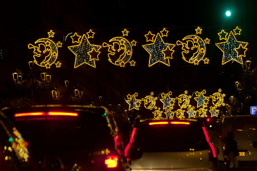Street  Christmas lights decorations, tinsel, Vigo, Pontevedra province, Galicia, Spain. Group of red tail car lights in the lower part of the image, traffic jam.