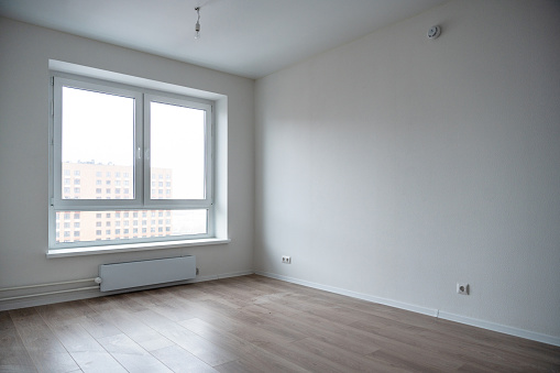 An empty room interior an apartment building. Window, white walls and light beige wooden laminate on the floor