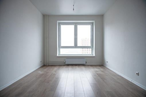 An empty room interior an apartment building. Window, white walls and light beige wooden laminate on the floor