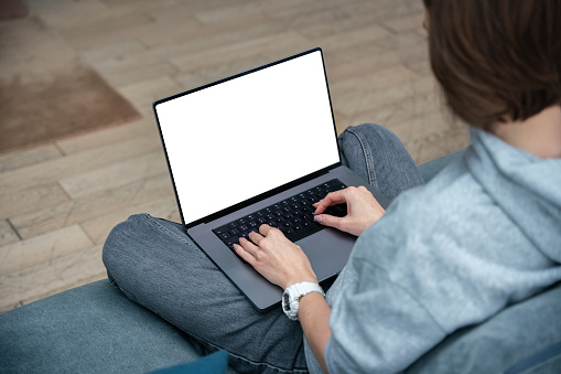 Woman sitting on the sofa with a laptop with blank white screen and surfing the net