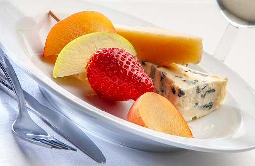 Cheese and fruit  on a white plate, close-up.