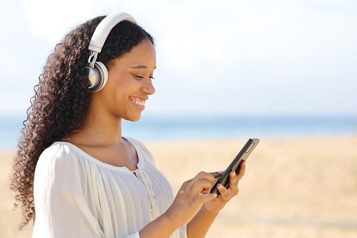 Happy black woman using cell phone on the beach