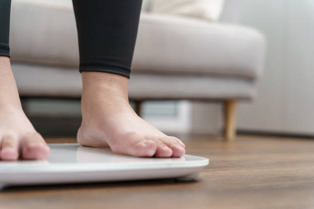 istock Fat diet and scale feet standing on electronic scales for weight control. Measurement instrument in kilogram for a diet control. 1803640166