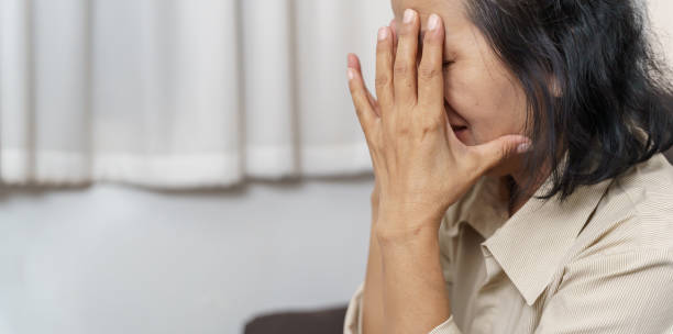 istock Sad middle age Asian woman touching forehead having headache suffering from migraine. matureÂ asian woman feeling sickÂ or depression. 1803646926