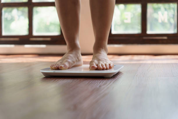 istock Fat diet and scale feet standing on electronic scales for weight control. Measurement instrument in kilogram for a diet control 1803649737