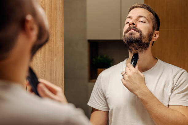 reflection of a man trimming his beard in a bathroom in front of the mirror. - shaving men electric razor reflection imagens e fotografias de stock