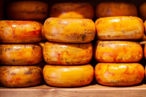 Multiple cheese wheels piled high on a shelf in a market in Amsterdam, Netherlands