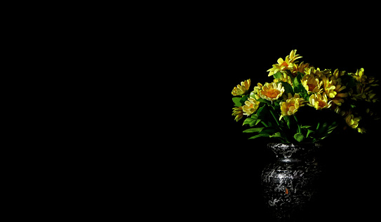 artificial yellow flowers in a vase on black background