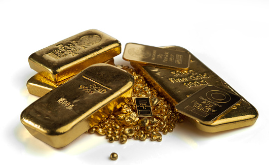 Several gold bars of different weights and a pile of gold granules. Selective focus. Isolated on a white background.
