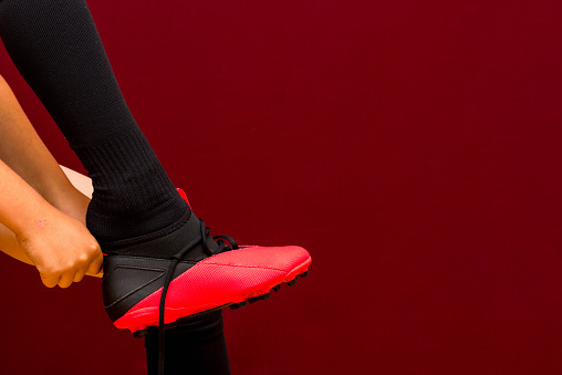 fragment of legs Young caucasian soccer kit socks soccer shoes red background.Copy space.