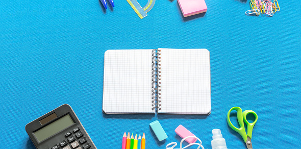 Blank graphing paper notebook with school supplies frame against a bright blue background. Back to school concept. Copy space.banner.advertisement.