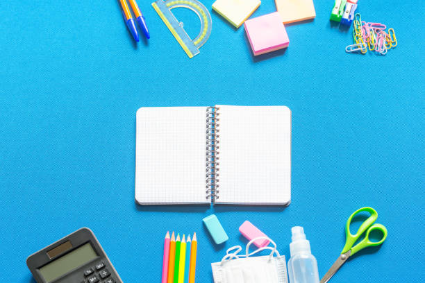 istock Blank graphing paper notebook with school supplies frame against a bright blue wall. Copy space.banner.advertisement. 1803703822