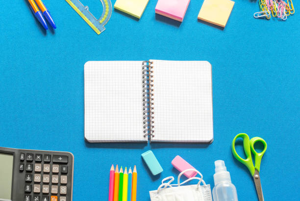 istock Blank graphing paper notebook with school supplies frame against a bright blue wall. Copy space.banner.advertisement. 1803703830