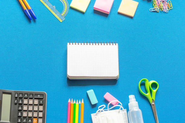 istock Blank graphing paper notebook with school supplies frame against a bright blue wall. Copy space.banner.advertisement. 1803703837