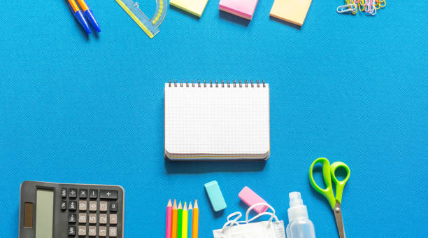 istock Blank graphing paper notebook with school supplies frame against a bright blue wall. Copy space.banner.advertisement. 1803703845