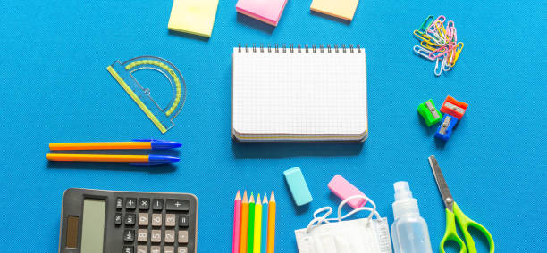 istock Blank graphing paper notebook with school supplies frame against a bright blue wall. Copy space.banner.advertisement. 1803704357