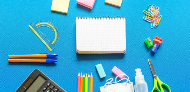 istock Blank graphing paper notebook with school supplies frame against a bright blue wall. Copy space.banner.advertisement. 1803704367