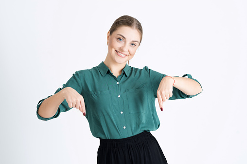 Attractive young woman points her fingers down at an empty copy space for advertising isolated on a white studio background. Advertises an interesting product for you.