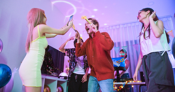 Un grupo de jóvenes amigos asiáticos millennials diversos con personas LGBTQIA+ bailan juntos en una fiesta en casa, celebran el Año Nuevo, la Navidad o el cumpleaños por la noche. Feliz evento de celebración, concepto de actividad divertida photo