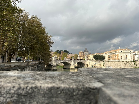 Timeless Rome as the sun sets, casting a warm glow on an ancient bridge spanning the tranquil Tiber River. This picturesque scene embodies the rich history and romantic allure of the Eternal CityT