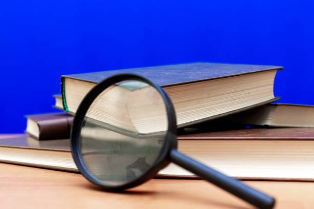 istock Magnifying glass a few closed books on a brown table blue background 1803740939