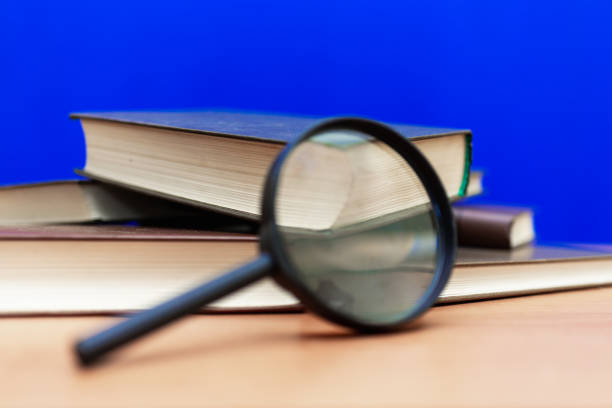 istock Magnifying glass a few closed books on a brown table blue background 1803740964