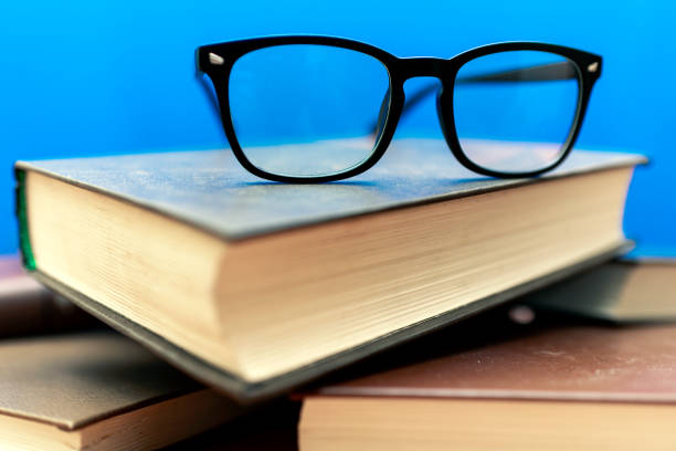 istock Books and eyeglasses on a wooden table, on blue soft background 1803740965
